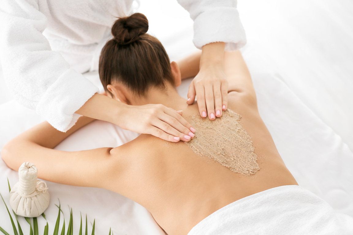 Young Woman Undergoing Treatment with Body Scrub in Spa Salon